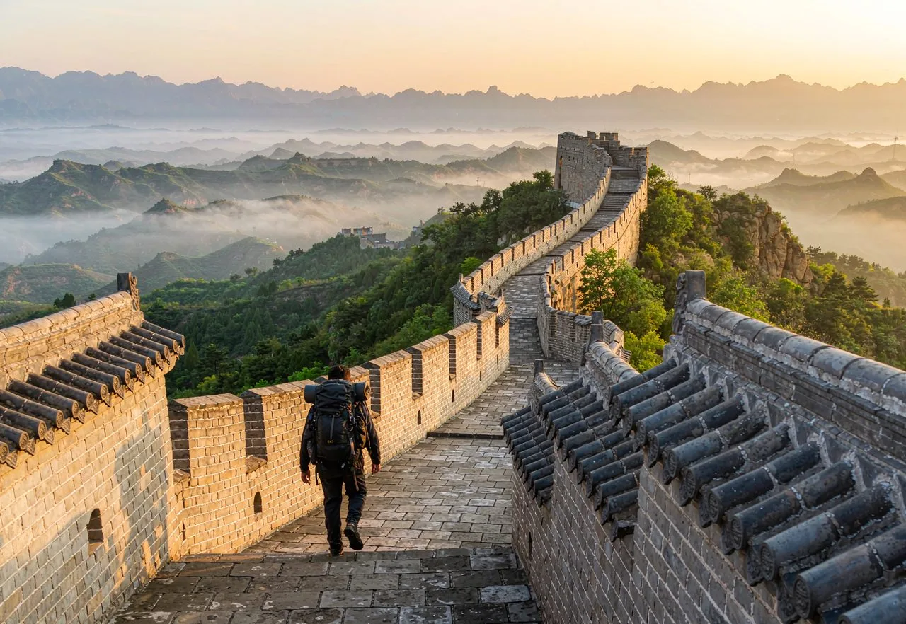 Backpacker with a backpack walking the Great Wall of China at sunrise