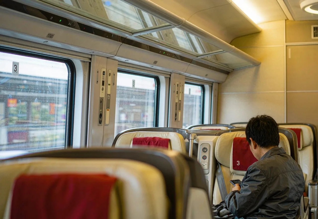 Inside a modern Chinese high-speed train carriage with large windows and a backpacker reading