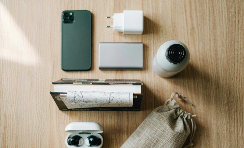 China travel essentials flat lay: passport, power adapter, power bank, smartphone, travel guidebook and earbuds on a wooden table