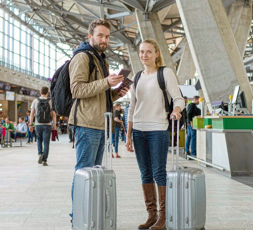 Two Western travelers with rolling suitcases and passports at a bright airport terminal, preparing for a trip to China
