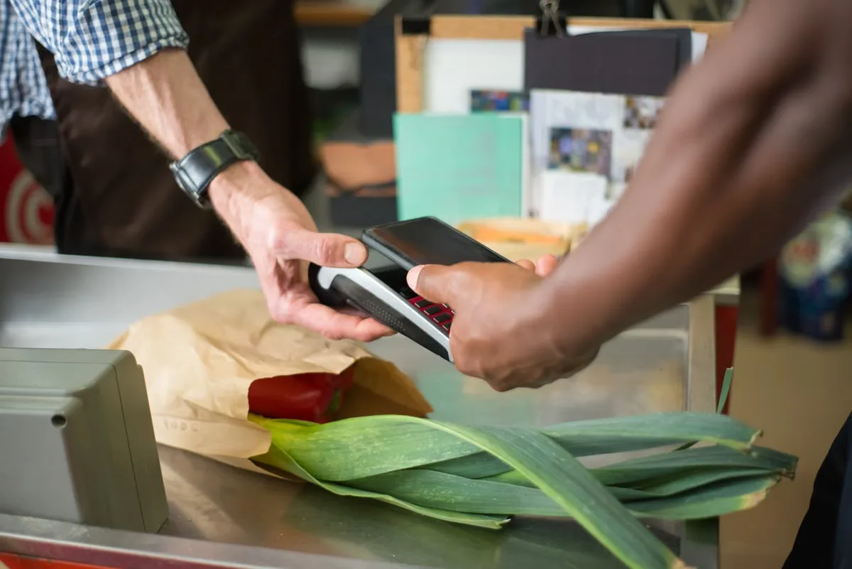 A shopper tapping a smartphone to pay at a grocery checkout