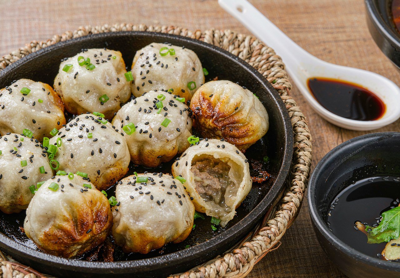 Pan-fried Shanghai shengjianbao in a cast-iron pan with sesame and scallions