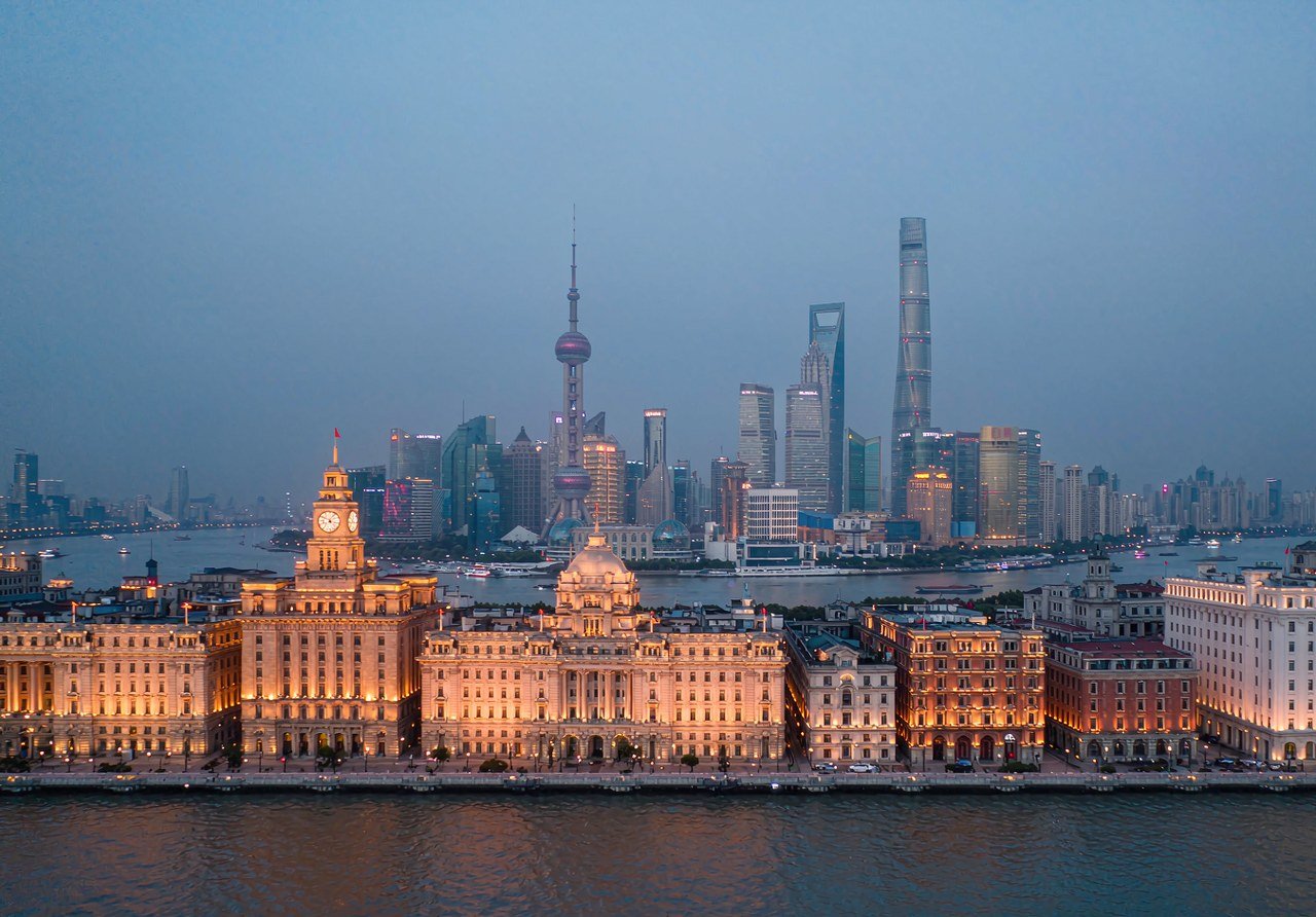 The Bund historic waterfront buildings lit at dusk with the Pudong skyline across the Huangpu River
