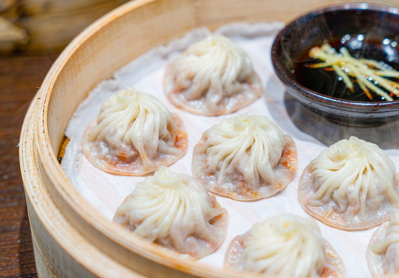 A bamboo steamer of Shanghai xiaolongbao soup dumplings with vinegar and ginger