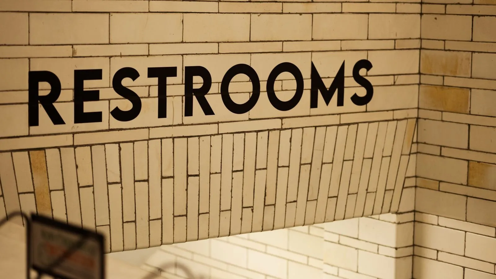 Restroom sign on a tiled wall inside a metro station