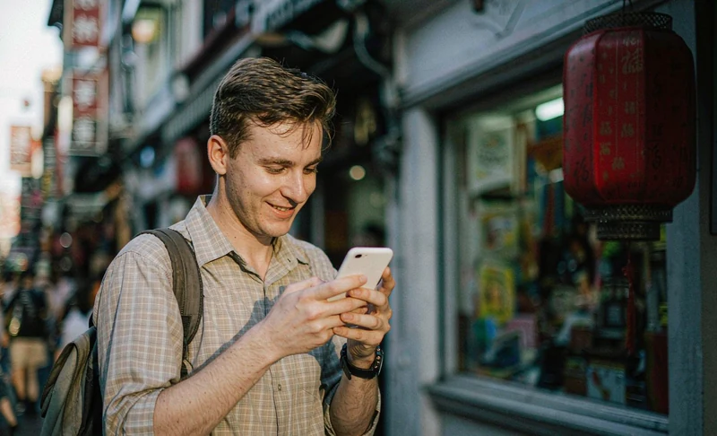A foreign tourist checking a smartphone on a busy street in China with a red Chinese lantern in the background